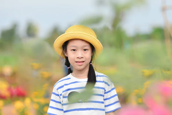 Cute Asian girl wearing yellow hat at flower field — Stock Photo, Image