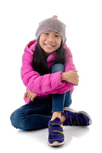 Happy Asian girl wearing pink down jacket sitting on white backg — Stock Photo, Image