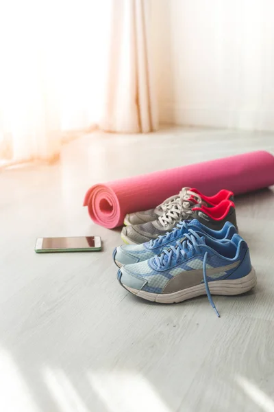 Брудне спортивне взуття на підлозі з йоги килимок і смартфон вдома — стокове фото