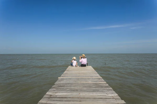 Two girl siiting on wooden pier facing to sea view and blue sky — Stock Photo, Image