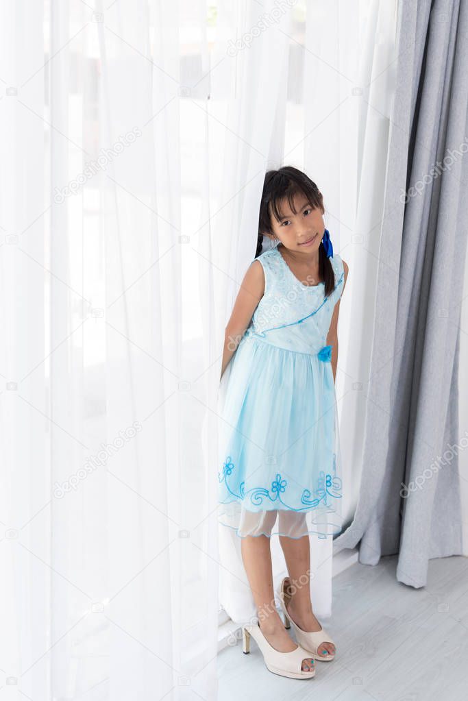 Cute Asian girl wearing her mother's high heel shoes standing ne