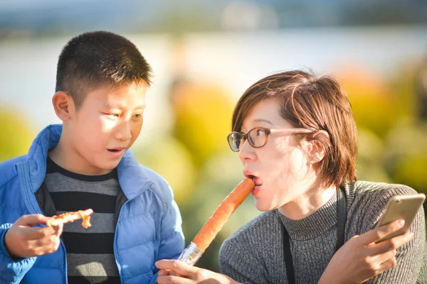Ásia menino alimentação salsicha para seu tia enquanto ela está usando inteligente p — Fotografia de Stock