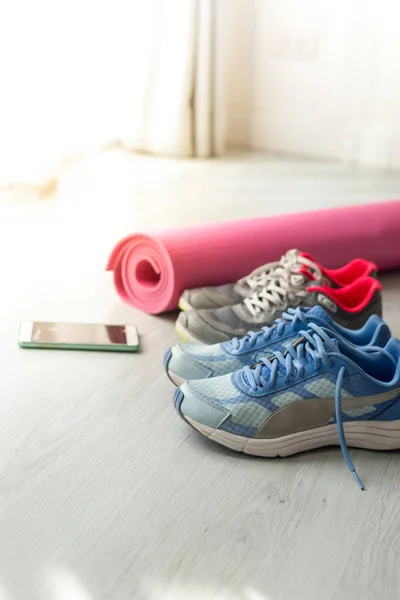 Брудне спортивне взуття на підлозі з йоги килимок і смартфон вдома — стокове фото