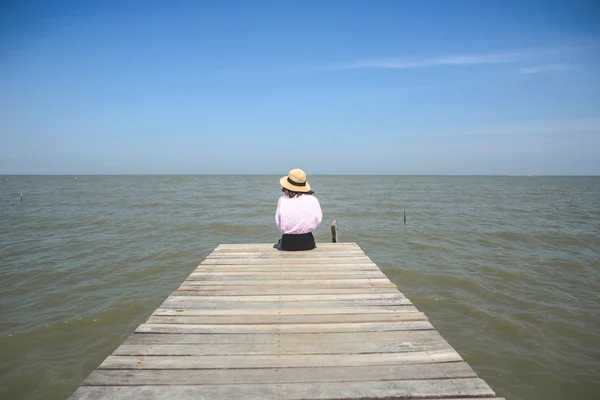 Indietro della ragazza che siede sul molo di legno di fronte alla vista sul mare e blu — Foto Stock