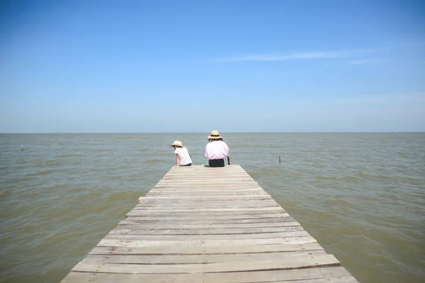 Two girld siiting on wooden pier facing to sea view and blue sky — Stock Photo, Image