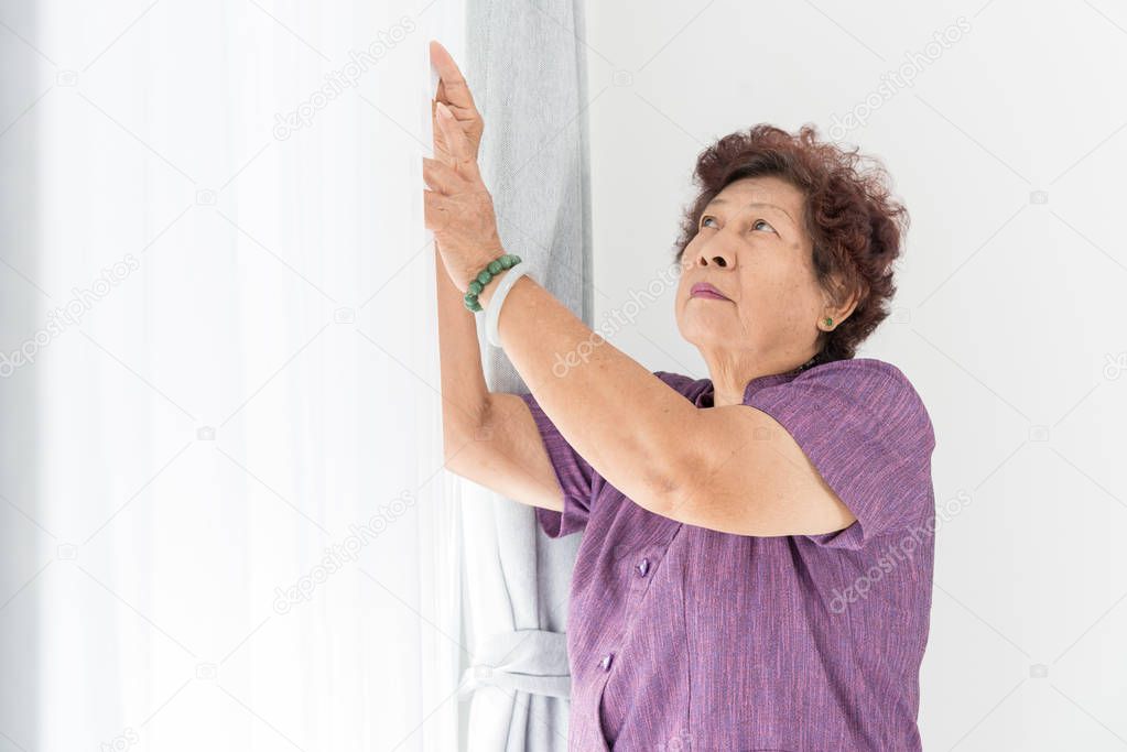 Asian senior woman close white curtain near window at home.
