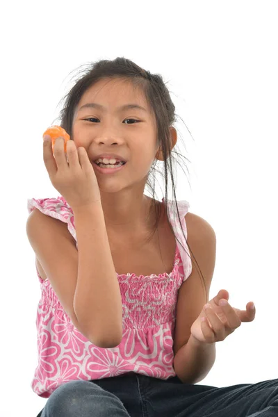 Asijská dívka jíst pomeranče a otevřít ústa na bílém pozadí. — Stock fotografie