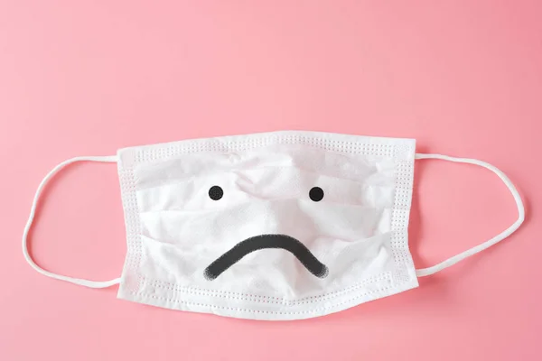 Unhappy face on Protective white face mask on pink background.