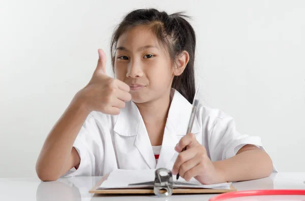 Girl in doctor costume working on table and thumb up. — Stock Photo, Image