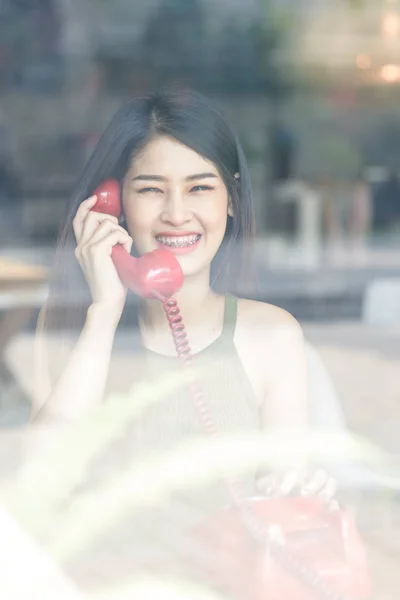 Glücklich asiatische Frau trägt Hosenträger und hält rote Vintage-Telefon, t — Stockfoto