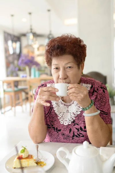 Asijské starší žena pít čaj v kavárně. — Stock fotografie