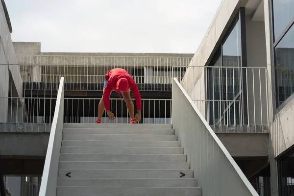 Sportmann mit roter Kapuze macht Bewegung auf Stufen im Freien. — Stockfoto
