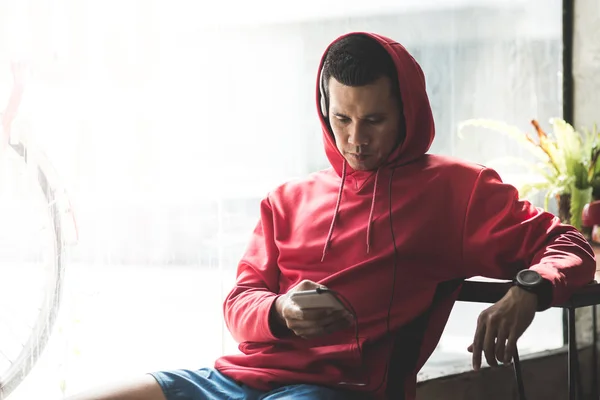 Sport man in red hood listening to music by smart phone, modern