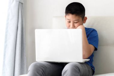 Kanepede oturan ve evde dizüstü kullanarak Asya çocuk.