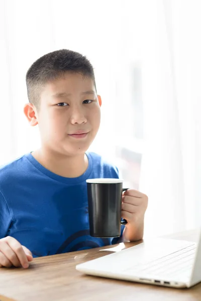 Felice asiatico ragazzo holding nero tazza mentre utilizzando tablet a casa . — Foto Stock