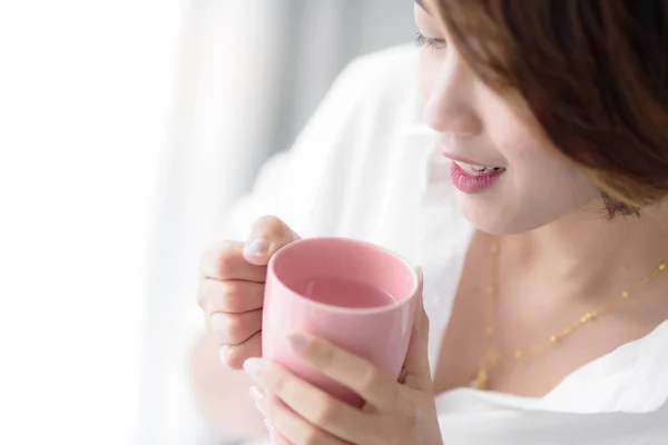 Vacker kvinna med rosa kopp nära fönstret hemma. — Stockfoto