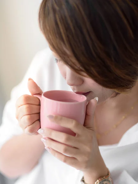 Hermosa mujer sosteniendo taza rosa cerca de la ventana en casa . —  Fotos de Stock