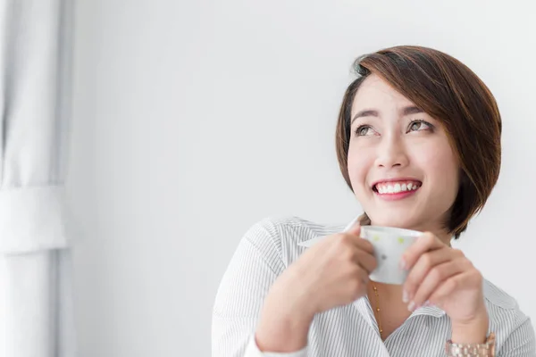 Feliz joven empresaria bebiendo té mientras está sentada en la silla en —  Fotos de Stock