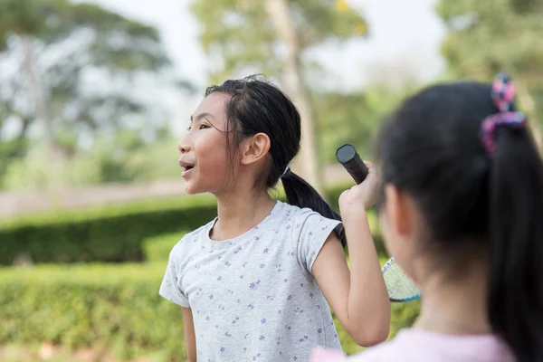 Felice ragazza asiatica tenendo badminton e parlando con un amico . — Foto Stock