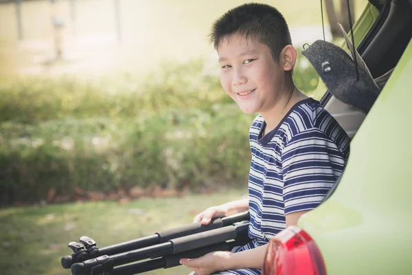 Asian boy sitting in rear door car and holding tripod, lifestyle — Stock Photo, Image