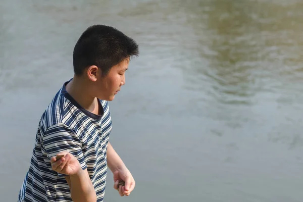Asiatischer Junge wirft Stein ins Wasser, Outdoor-Lebensstil. — Stockfoto