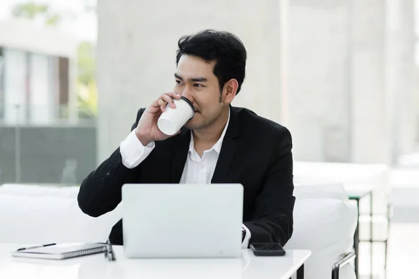 Asijský podnikatel pití kávy a práce s přenosným počítačem v kavárně o — Stock fotografie