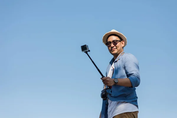 Happy asijské turisty pomocí fotoaparátu stick pořízení fotografie s modrým sk — Stock fotografie