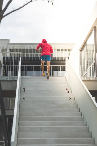 Rücken des Sportlers in roter Kapuze, der an Stufen hochläuft, Bewegungsunschärfe. — Stockfoto