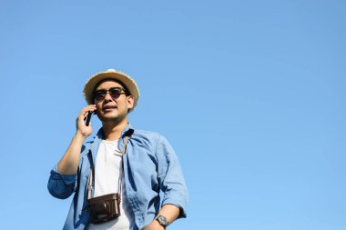 Turist Asya adam cep telefonu mavi gökyüzü ile yaz aylarında konuşurken.