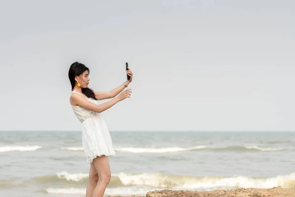 Mujer hermosa feliz usando smartphone para selfie en la playa . — Foto de Stock