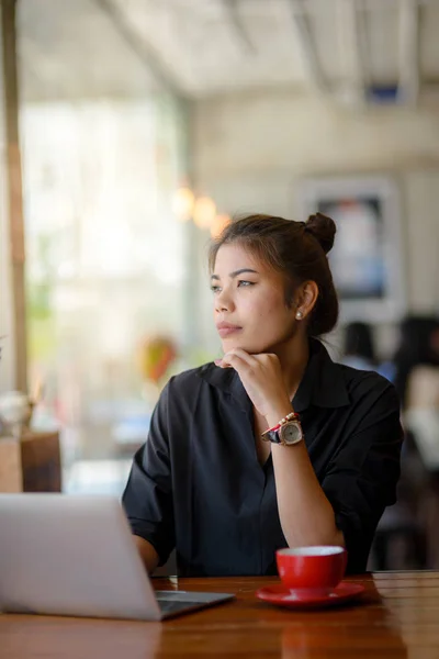 Mujer asiática trabajando en la cafetería y mirando por la ventana . — Foto de Stock