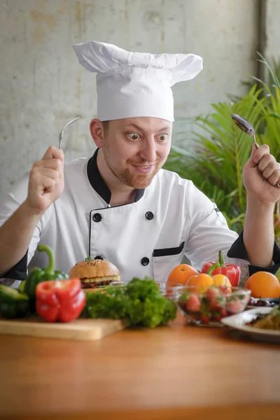 Estressado chef profissional segurando colher e garfo com vegetais — Fotografia de Stock