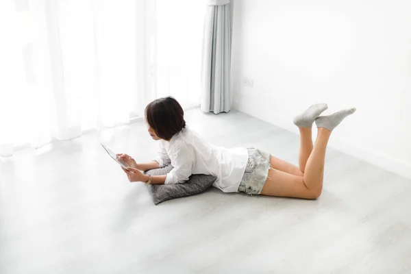 快乐亚洲妇女使用片剂和躺在地板上在家 — 图库照片