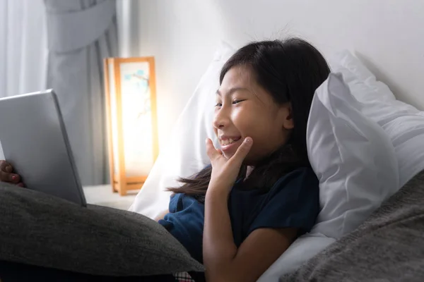 Glad asiatisk tjej använda surfplatta på säng hemma med svagt ljus. — Stockfoto