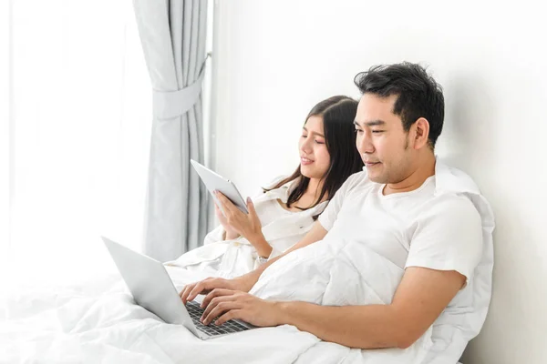 Feliz ásia casal usando laptop e tablet juntos no cama no ho — Fotografia de Stock