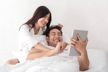 Dizüstü ve tablet birlikte yatakta ho kullanarak mutlu Asya çift