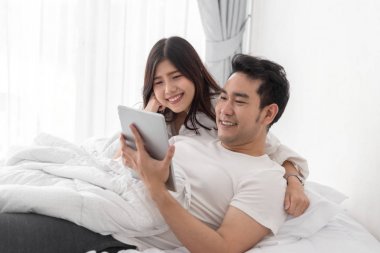 Dizüstü ve tablet birlikte yatakta ho kullanarak mutlu Asya çift