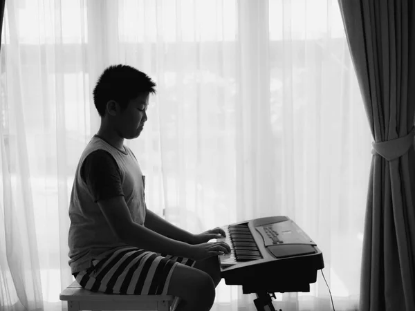 Asiatiska boy spela keyboard piano hemma, svart och vitt. — Stockfoto