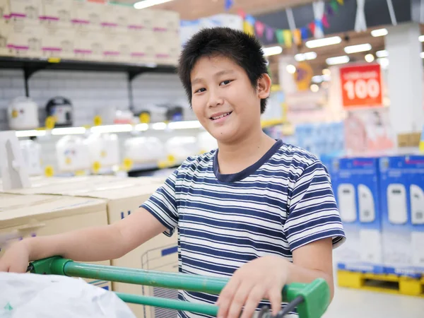 Happy preteen boy with shopping cart at supermarket. — Stock Photo, Image