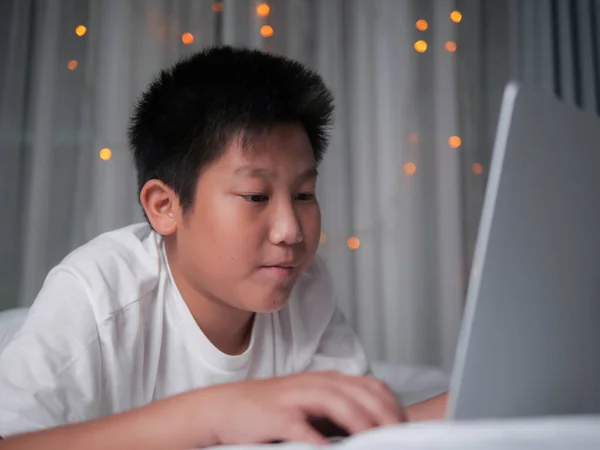 Happy preteen boy using laptop on bed with christmas light backg — Stock Photo, Image