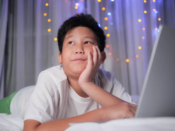 Happy preteen boy using laptop on bed with christmas light backg — Stock Photo, Image