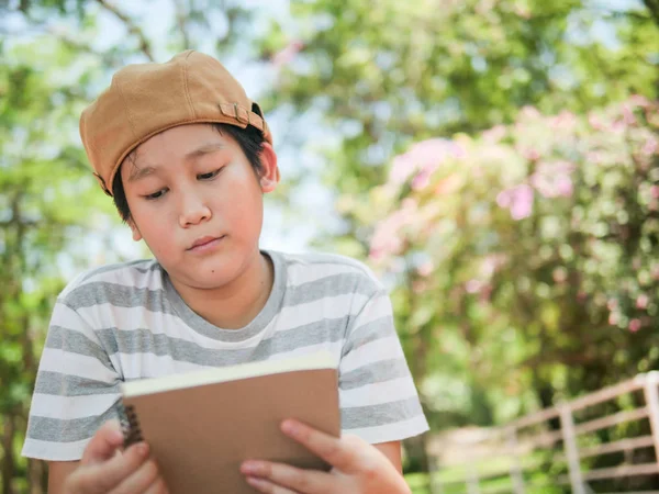 Glad asiatiska preteen pojke läser en bok som är utomhus. — Stockfoto