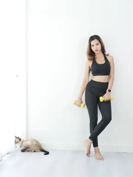 Asiática mujer ejercicio con dumbbell al lado de su gato en casa . — Foto de Stock