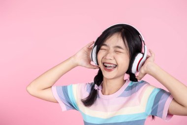 Happy Asian teenager girl using headphone on pink background.