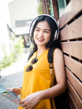 Sırt çantalı Asyalı kadın kulaklık takıyor ve haritayı tutuyor.