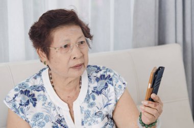 Kanepede akıllı telefon kullanan Asyalı son sınıf öğrencisi bir kadın. Yaşam tarzı kavramı.