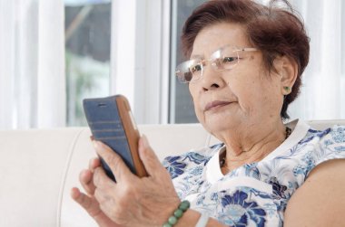 Kanepede akıllı telefon kullanan Asyalı son sınıf öğrencisi bir kadın. Yaşam tarzı kavramı.