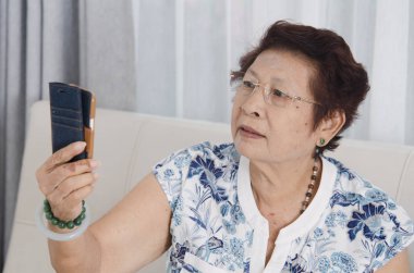 Kanepede akıllı telefon kullanan Asyalı son sınıf öğrencisi bir kadın. Yaşam tarzı kavramı.