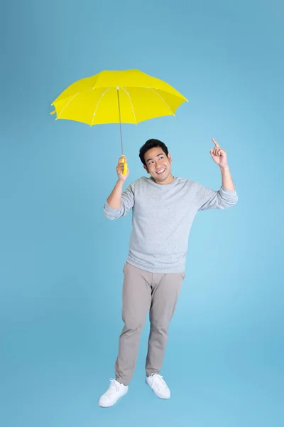 Feliz ásia homem segurando amarelo guarda-chuva no azul fundo . — Fotografia de Stock