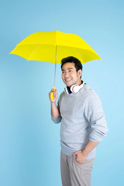 Asiatico uomo holding giallo ombrello con blu sfondo . — Foto Stock